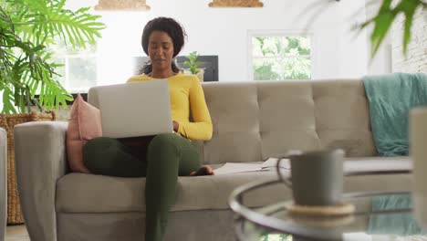 Video-of-happy-african-american-woman-sitting-on-sofa-using-laptop