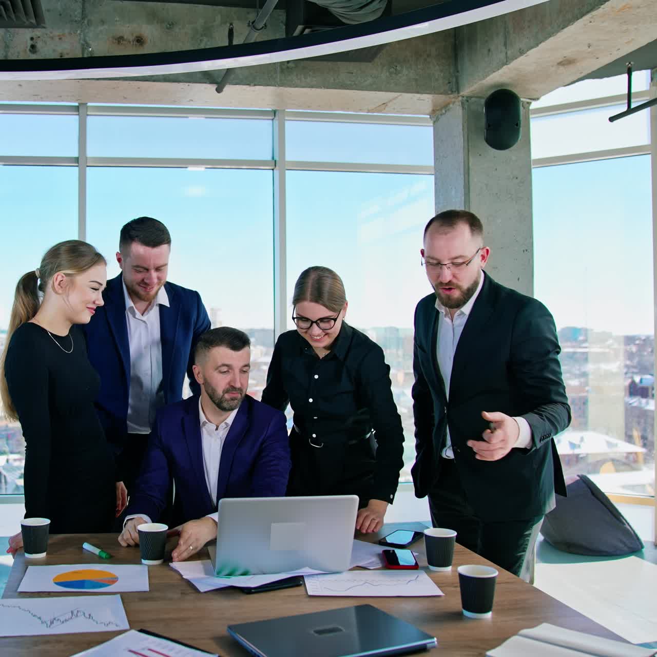 Teamwork of business people. Group of young entrepreneurs men and women use laptop and talk together in modern office. Panoramic window view with a city background