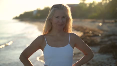 Cámara-Lenta-De-Una-Mujer-Bastante-Madura-Retroiluminada-Sonriendo-A-La-Cámara-Y-Luego-Tirando-Su-Cabello-Y-Coqueteando-Mientras-Está-En-Una-Playa