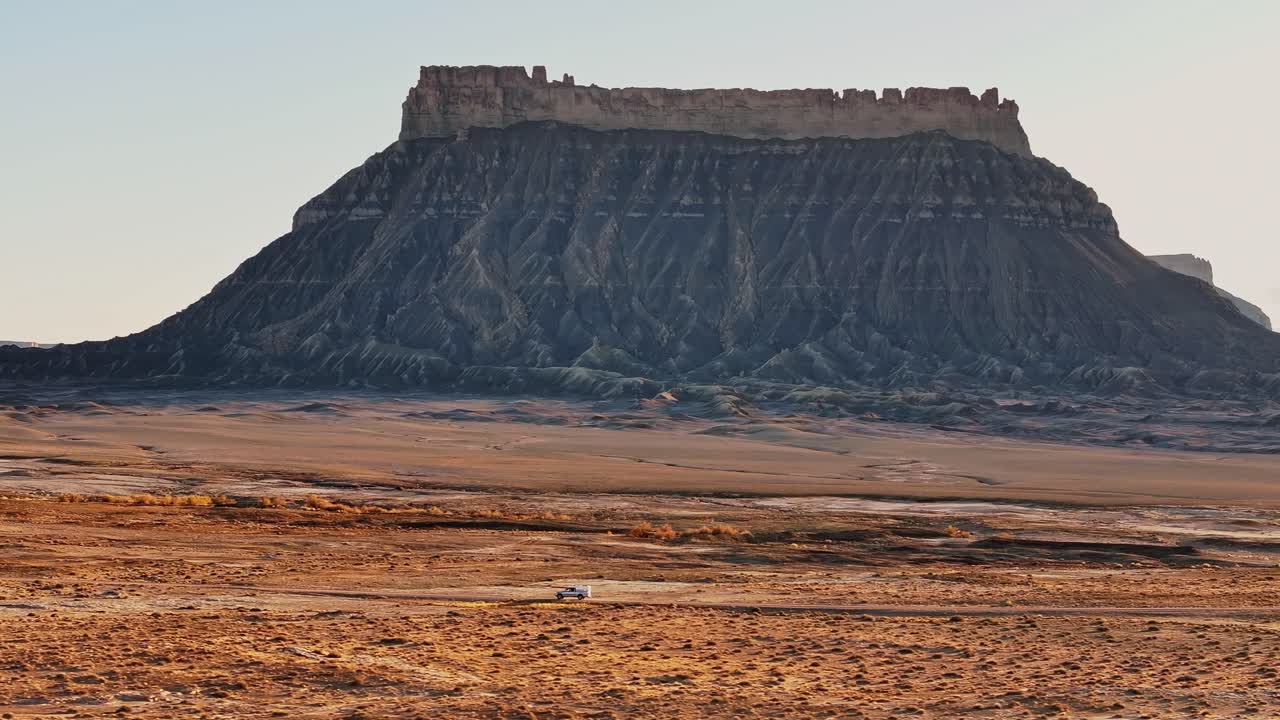 Mesa drammatica che si erge da un terreno desertico pianeggiante vicino al paesaggio di Hanksville, Utah, con un camper che guida lungo una strada sterrata.