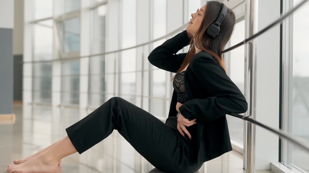 una joven elegante con auriculares sentada junto a la ventana disfruta de la música