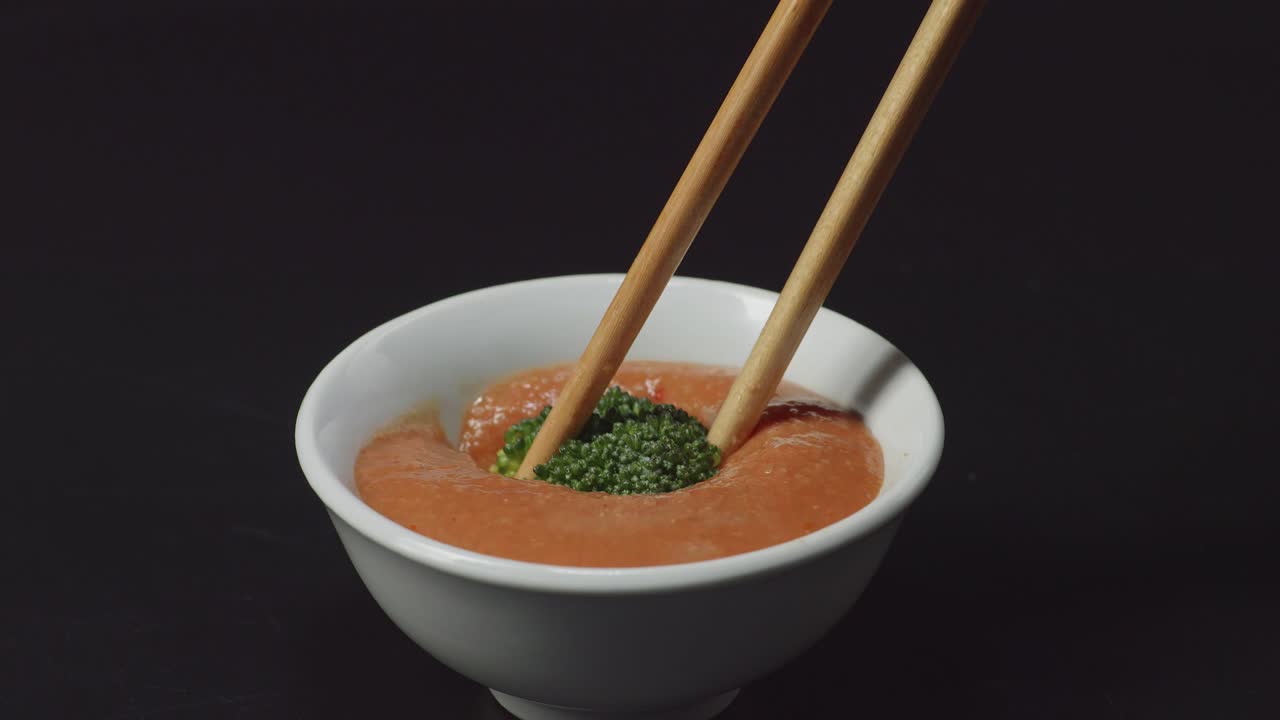 up de brócoli sumergiendo a la salsa de sumergir shabu shabu por palillos en el fondo negro