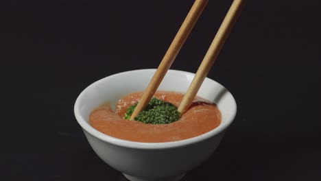 up de brócoli sumergiendo a la salsa de sumergir shabu shabu por palillos en el fondo negro