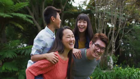 smiling asian father and mother piggy backing happy son and daughter in garden