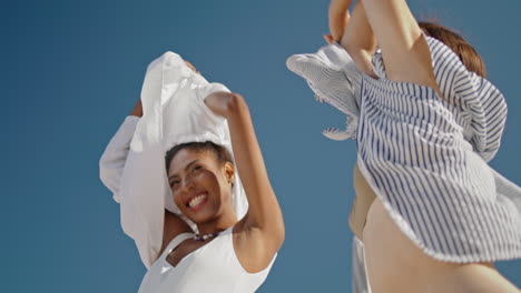 Beach-girls-taking-shirts-off-at-shore-closeup.-Beautiful-happy-friends-relaxing