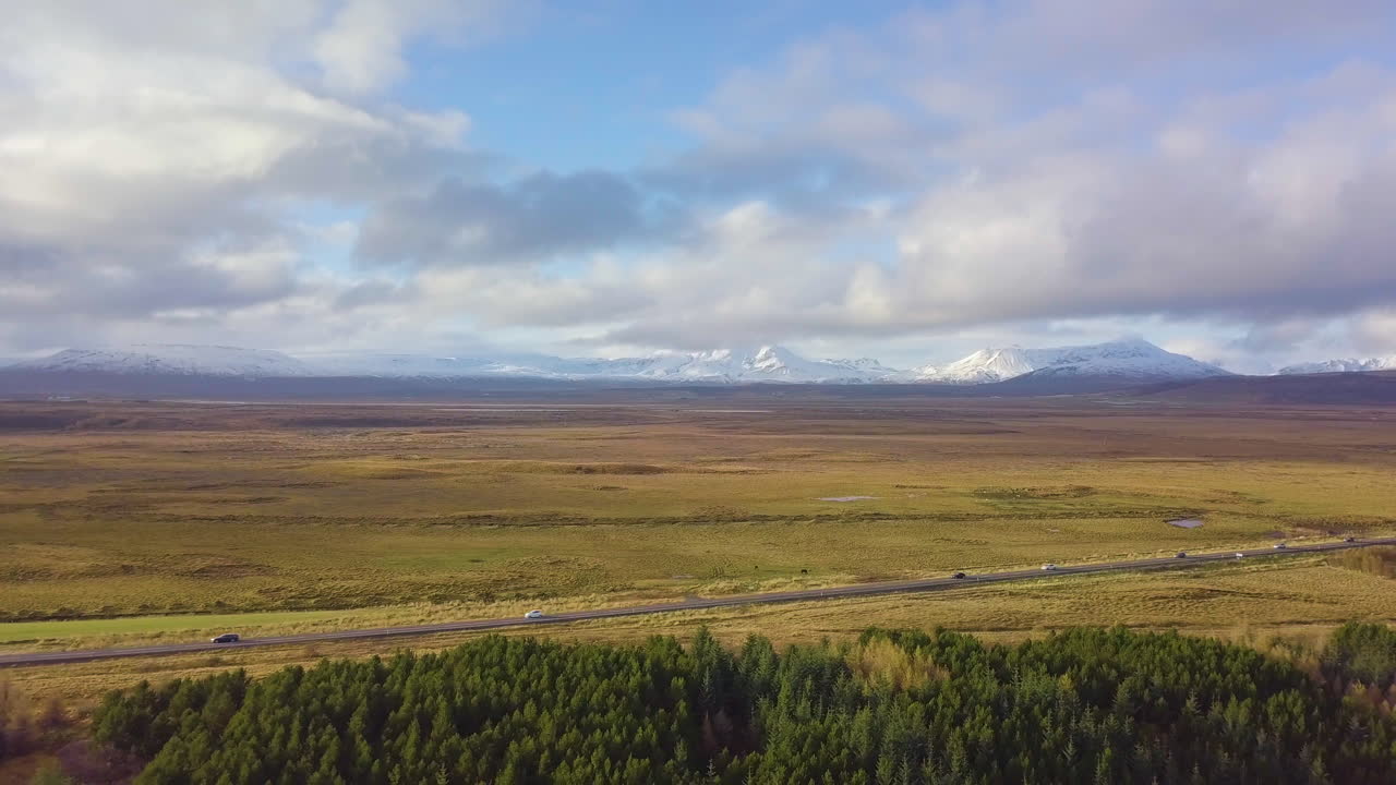 Vista de drone de carros circulando em uma estrada com campos e montanhas ao fundo na Islândia