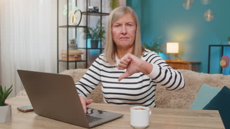 mature woman working reading negative comment on laptop giving thumbs down dislike dissatisfaction