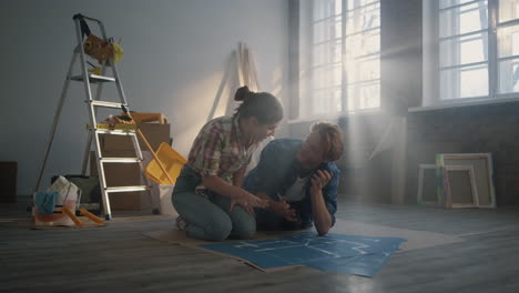 cheerful couple planning home repair inside. happy family sitting on floor.