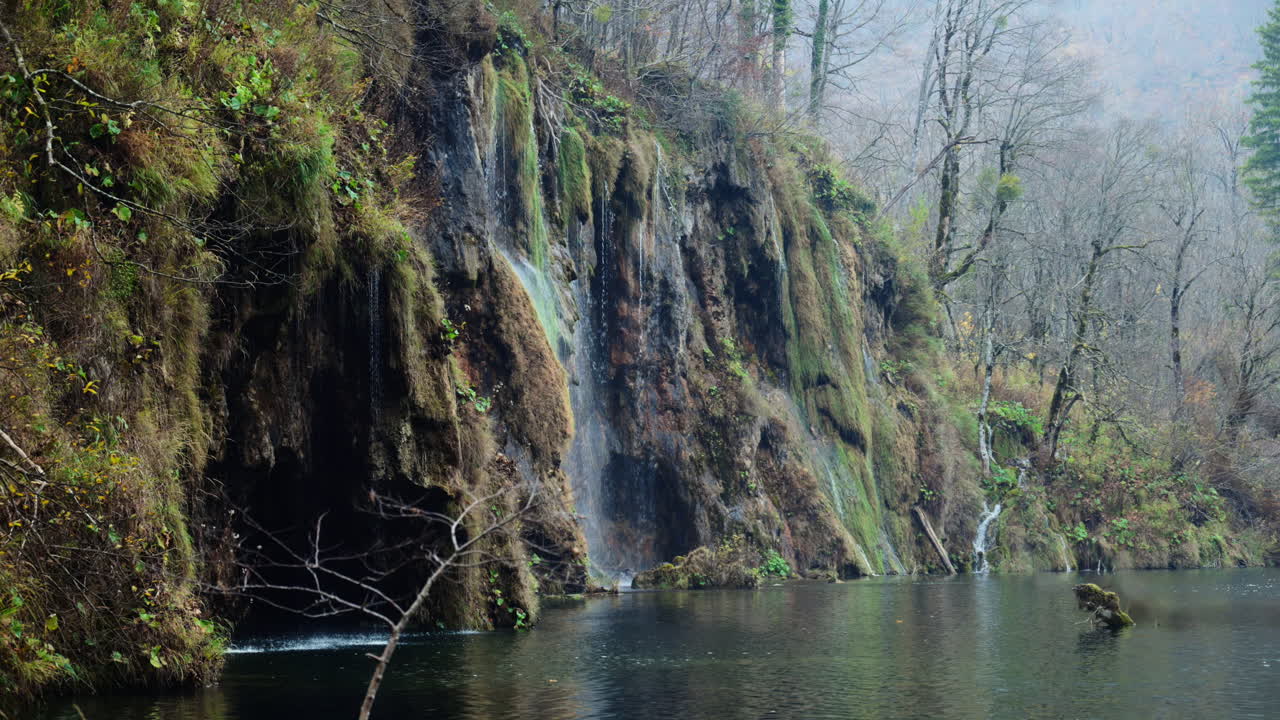 Vand, der strømmer over mosklædte travertinklipper ned i en rolig sø om efteråret. Plitvice Søerne Nationalpark, Kroatien