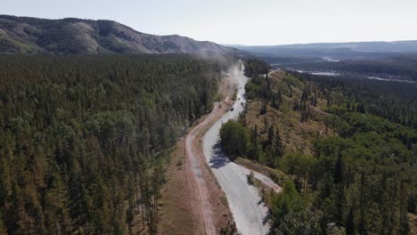 Multiple-cars-driving-along-a-dusty-logging-road-that-leads-through-boreal-forests-near-Ghost-River,-Alberta