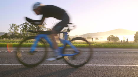 fast cyclist riding bike fast on road past countryside background with fog and morning sunlight, 4k slow motion