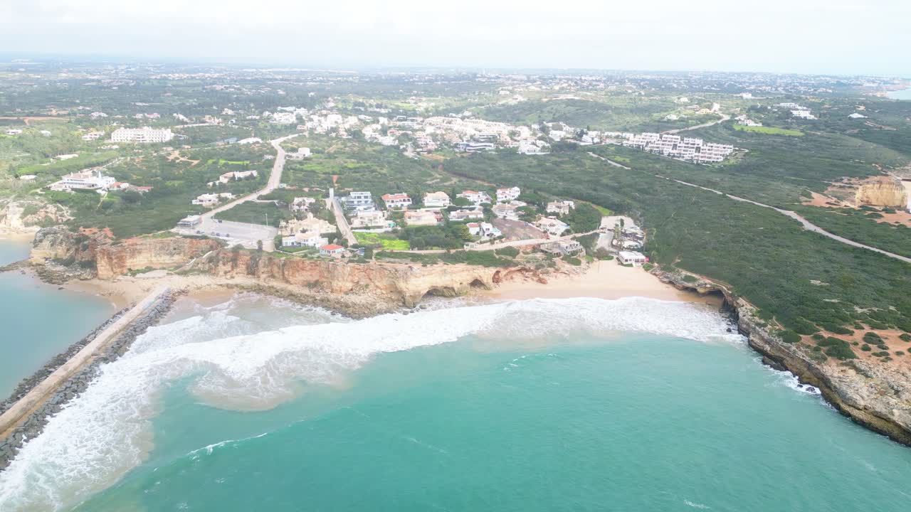 Ferragudo algarve coast with waves hitting beach and cliff homes, aerial view