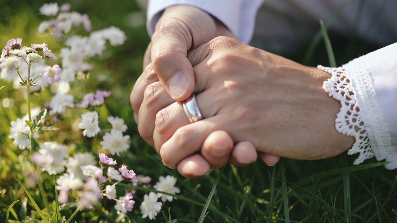 Adjusting woman shifting hands on lawn, angling ring catching sunlight, lace cuff near flowers