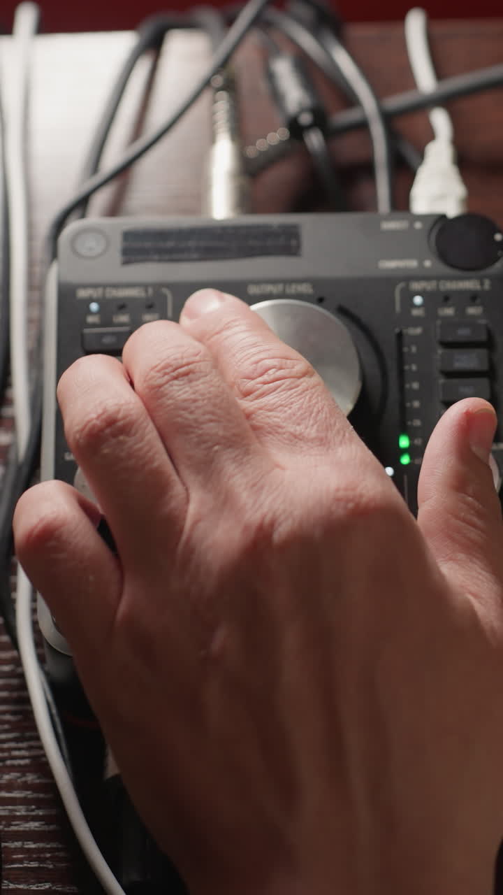 toma de primer plano de una mano que opera un mezclador de sonido, girando su perilla para ajustar los niveles de audio. la escena captura el control preciso y la habilidad técnica requerida en la ingeniería de sonido