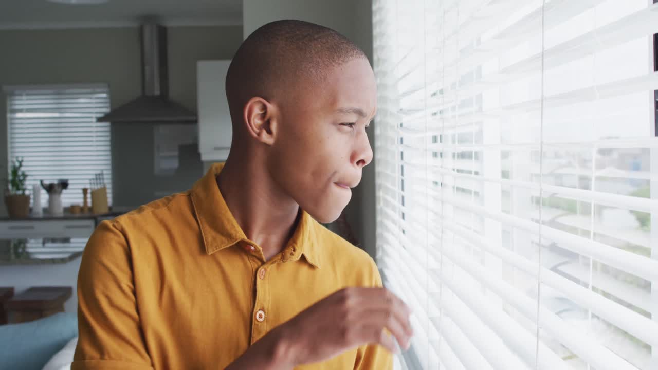 Video of sad african american boy looking outside window