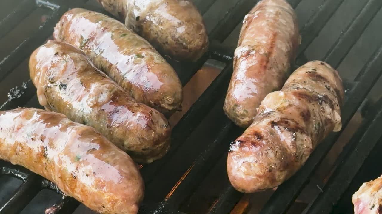 Sausages sizzle on outdoor barbecue grill, flames and smoke rising, close-up, natural daylight