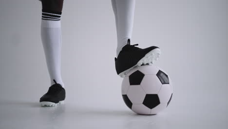 close-up of the foot of a professional black football player standing on the ball in slow motion in the white background. brazilian football player foot on the ball to pose