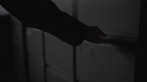 Person opening a file drawer in a dark office