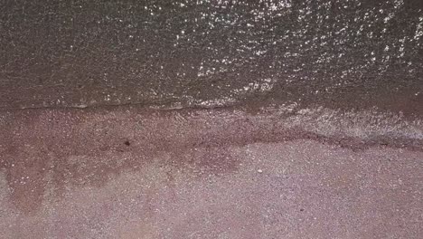 aerial bird's eye view of shimmering waves lapping onto a pebble beach, static crop