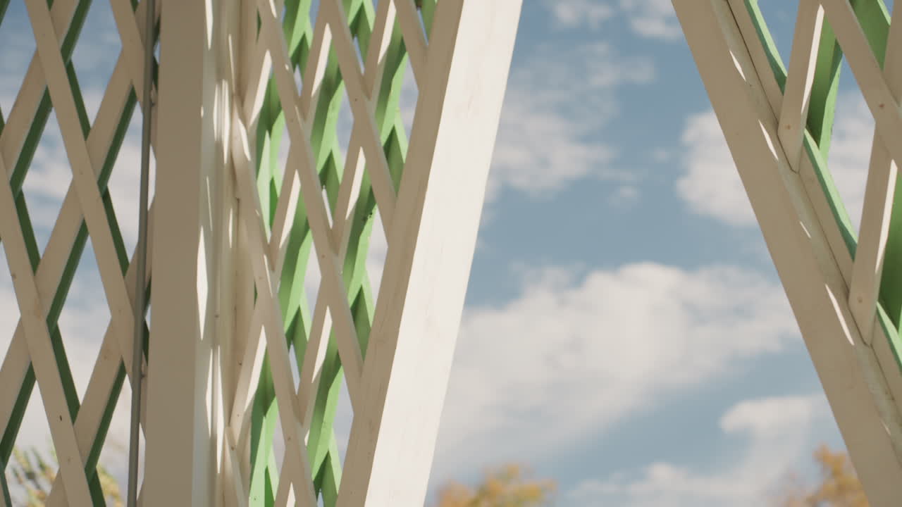 Pavilhão moderno sob céus ensolarados. Céu de verão com painéis de treliça nítidos e sombras suaves. Evento familiar íntimo realizado em jardim elegante com pavilhão moderno e jogo de sombras sutil.