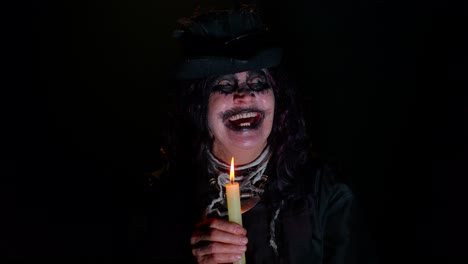 sinister old mature woman in carnival costume of halloween witch making magic rituals with candle