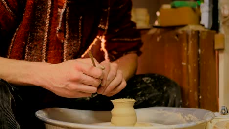 professional potter carving mug with special tool in pottery workshop