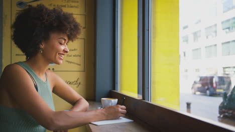 female customer in coffee shop window working writing in notebook