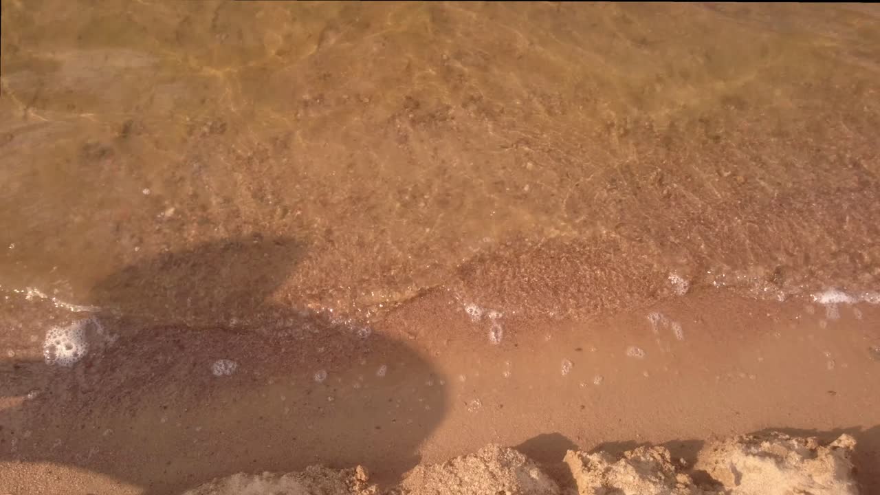 Lake water with playing child shadow. Sunshine at sand.