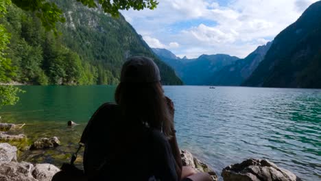 tourist woman taking a photo with a camera in a pebble beach by the shore of the king's lake, königssee in germany, bavaria