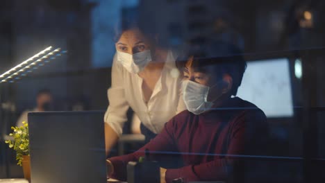 colegas con máscaras de seguridad discutiendo estadísticas mirando la pantalla de la computadora portátil trabajando hasta tarde en la oficina