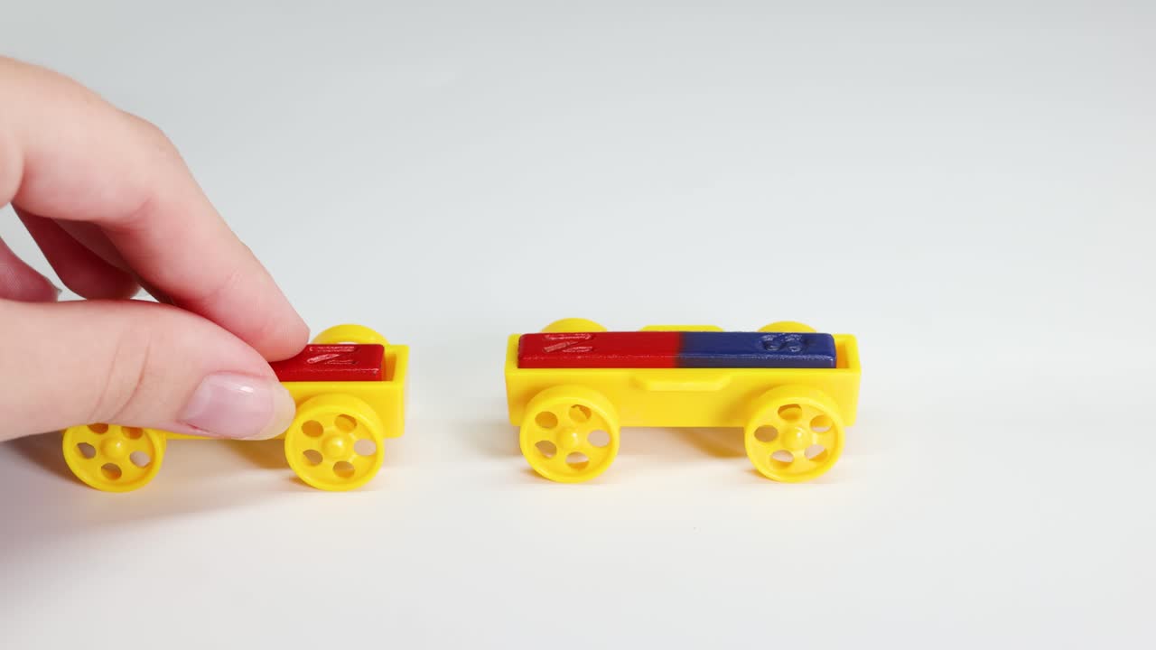Hands manipulate colorful toy cars with magnets, illustrating magnetic forces. Bright lighting and simple background enhance focus on interaction