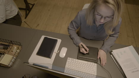 top view of a blonde female graphic designer drawing on a digital tablet at workplace