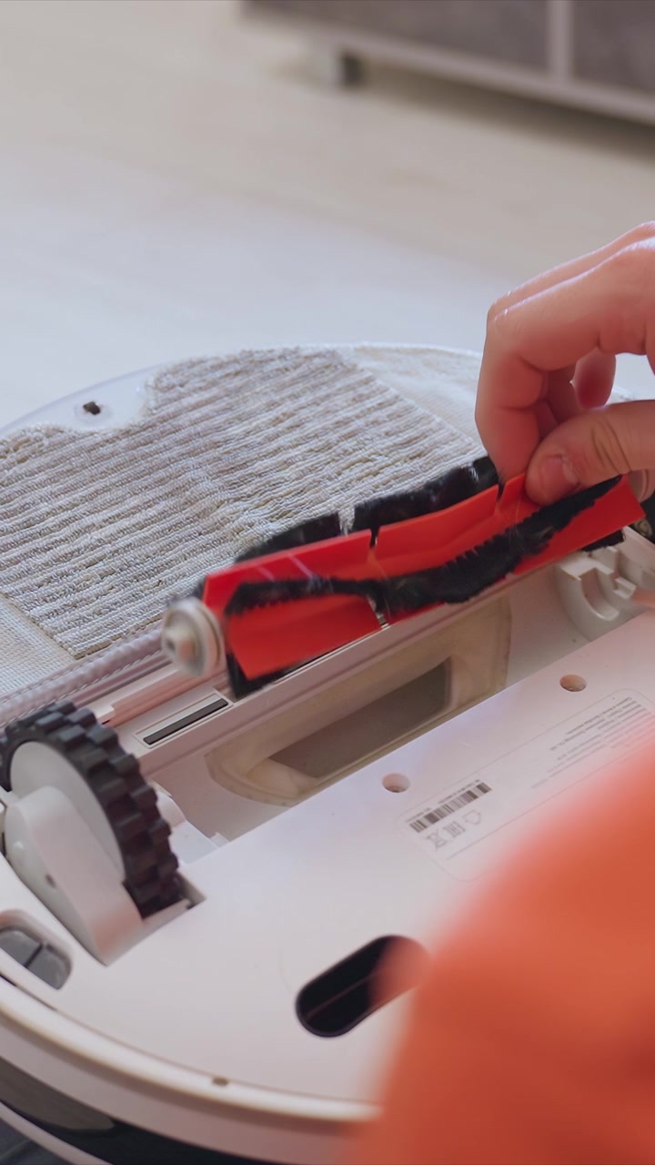 Person carefully removes and replaces brushes inside white robotic vacuum cleaner. focus is entirely on hands interacting with internal components demonstrating proper upkeep of home