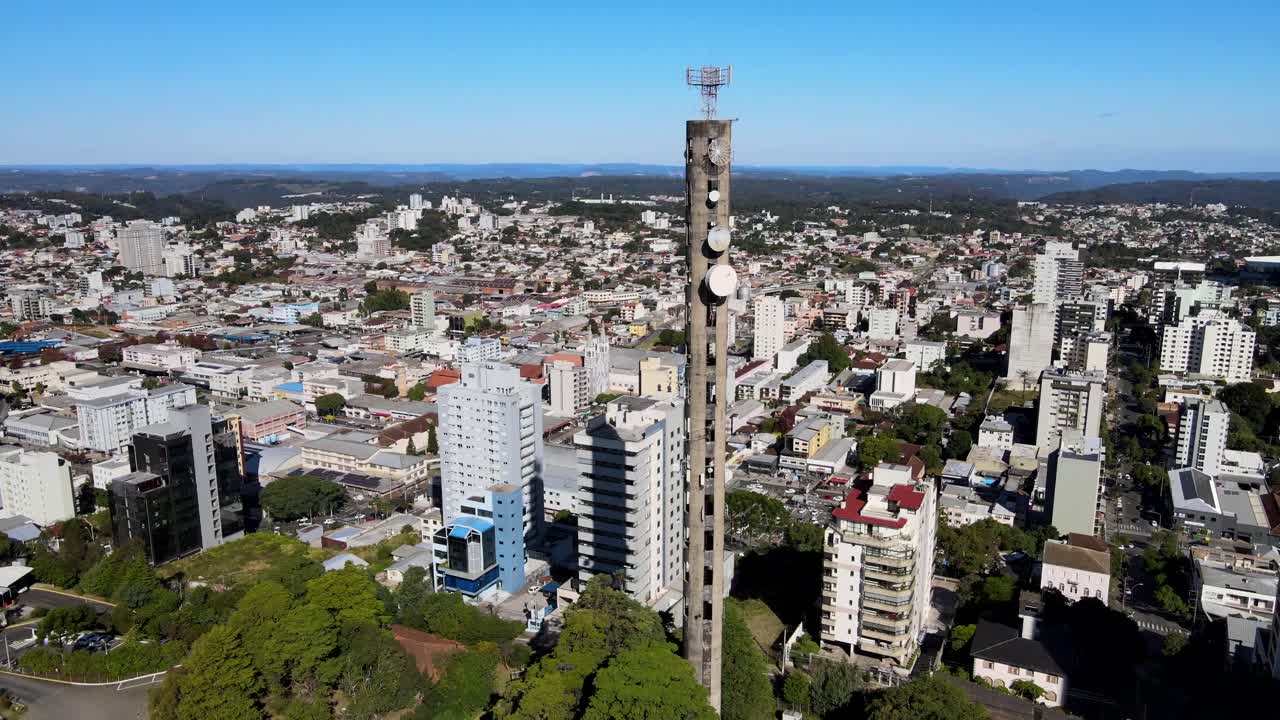 vista orbital aérea de una torre de teléfono celular de hormigón muy alta en el medio de una zona verde en una pequeña ciudad con muchos edificios bajo un día soleado