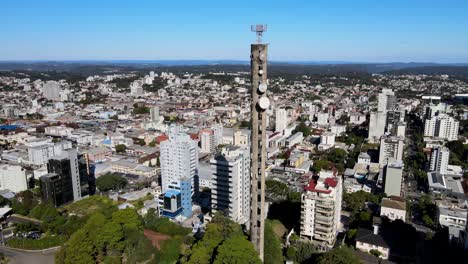 aerial orbital view of very tall concrete cell phone tower in the middle of a green area in a small city with many buildings under a sunny day