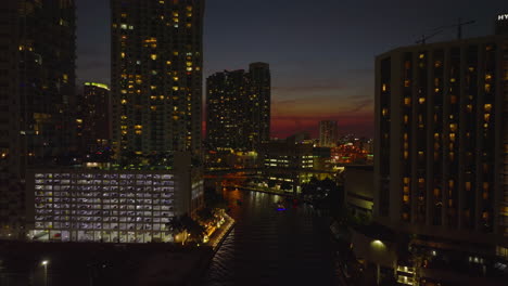 Backwards-fly-above-river-in-city.-Revealing-bridge-with-road-traffic.-Evening-view-against-twilight-sky.-Miami,-USA