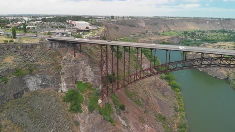 Inclinación-Aérea-Hacia-Arriba-En-Cámara-Lenta-De-Los-Vehículos-Que-Cruzan-El-Cañón-Del-Río-Snake-En-Twin-Falls,-Idaho-Con-La-Mitad-Del-Puente-Conmemorativo-De-Perrine-Enmarcado