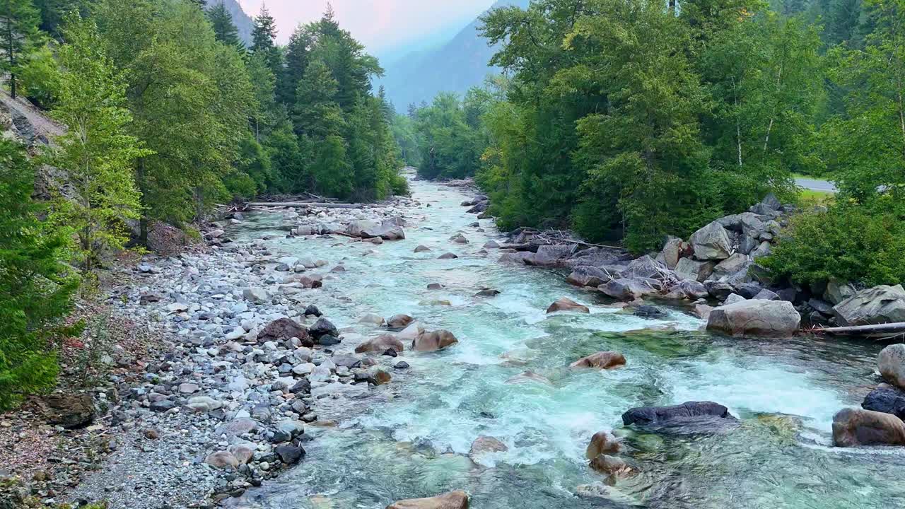 Drone che vola in retromarcia su un fantastico fiume alimentato da ghiacciai che attraversa un aspro paesaggio montano