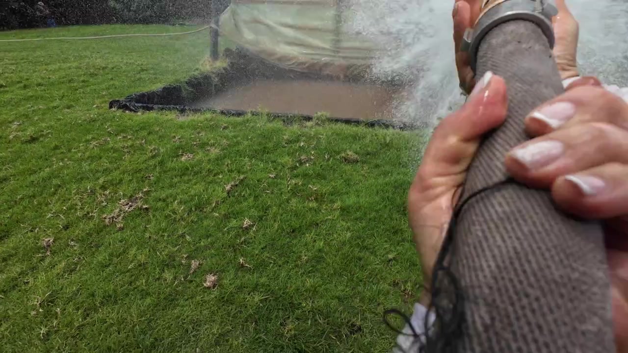 Mani di un pompiere che tengono una potente manichetta antincendio che spruzza acqua durante un'esercitazione all'aperto