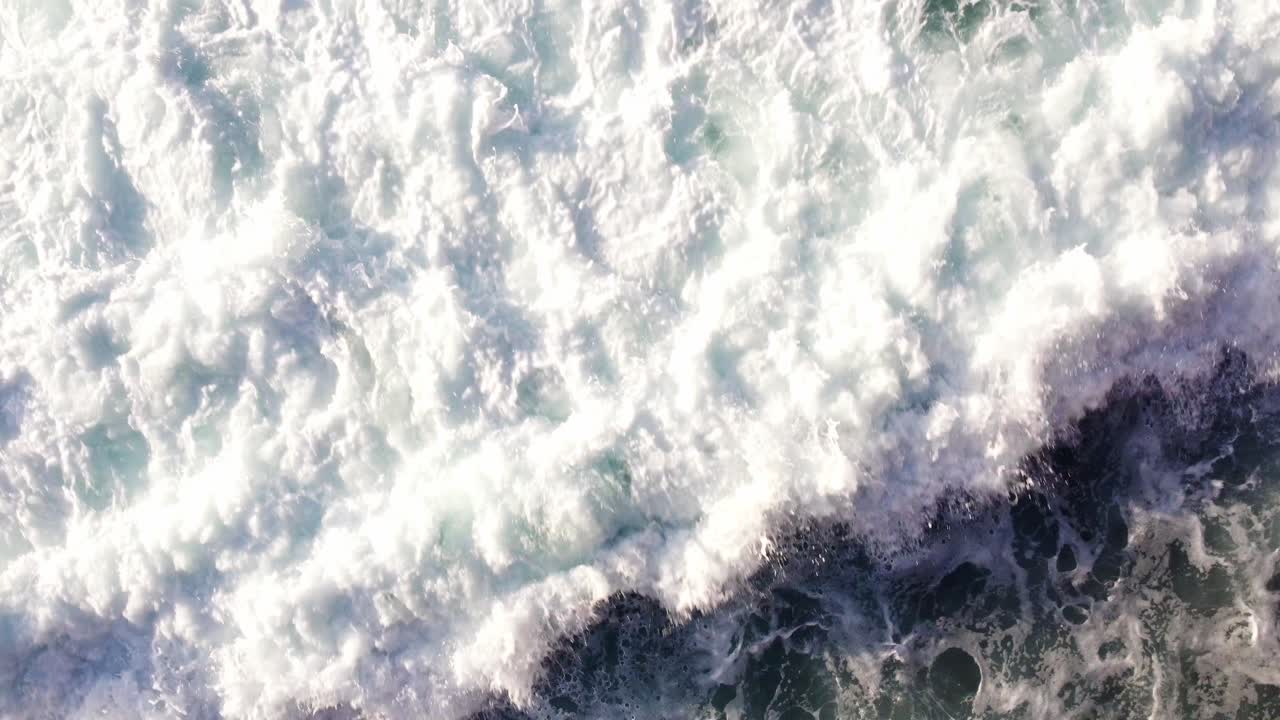 Vista aerea dall'alto di onde marine agitate che presentano un motivo superficiale di schiuma bianca