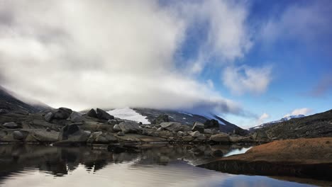 timelapse of clouds partly covering a mountain in norway, with pond in foreground