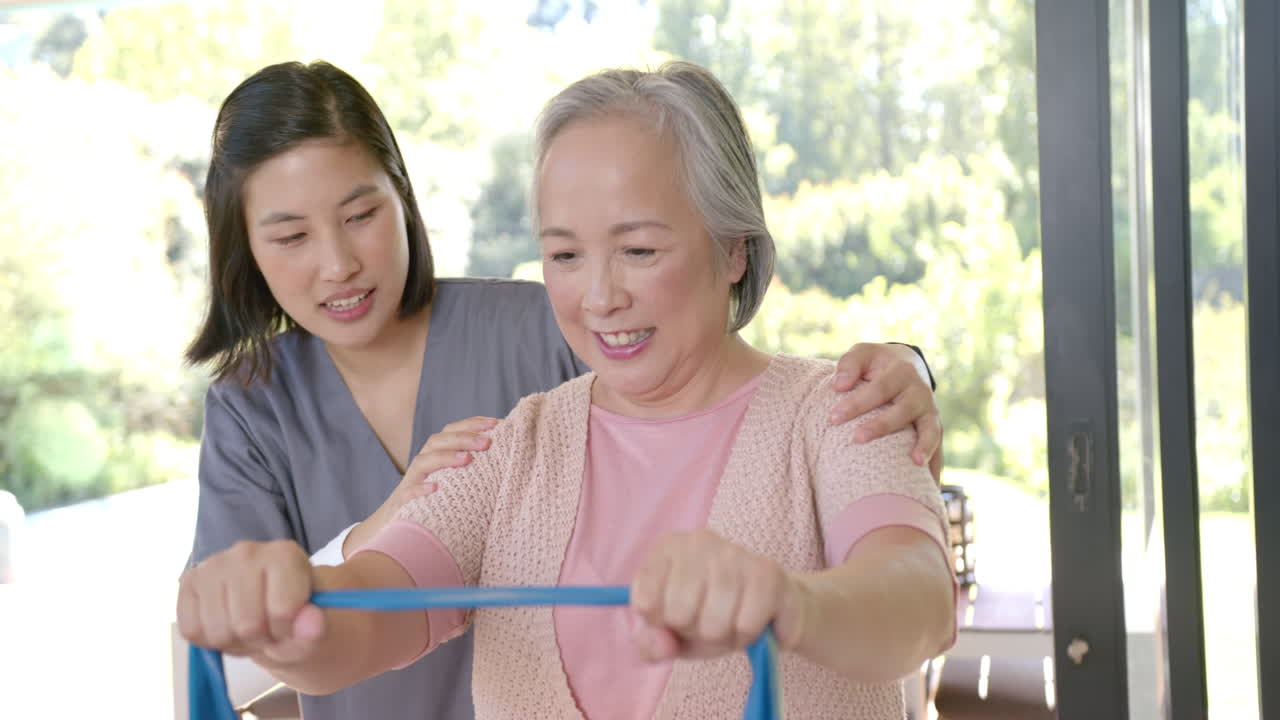 Assisting senior asian woman with resistance band exercises, physical therapist supporting