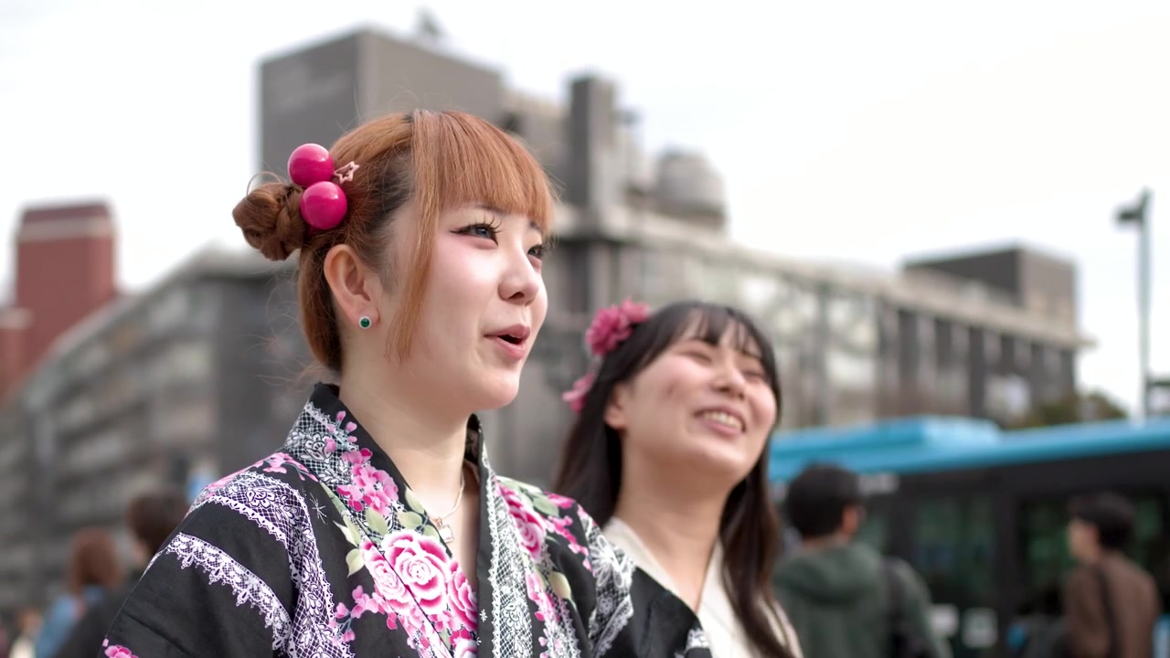 Geleneksel çiçekli kimonolar giymiş iki genç kadın, birlikte gülerken bir Tokyo sokağında yürüyor.