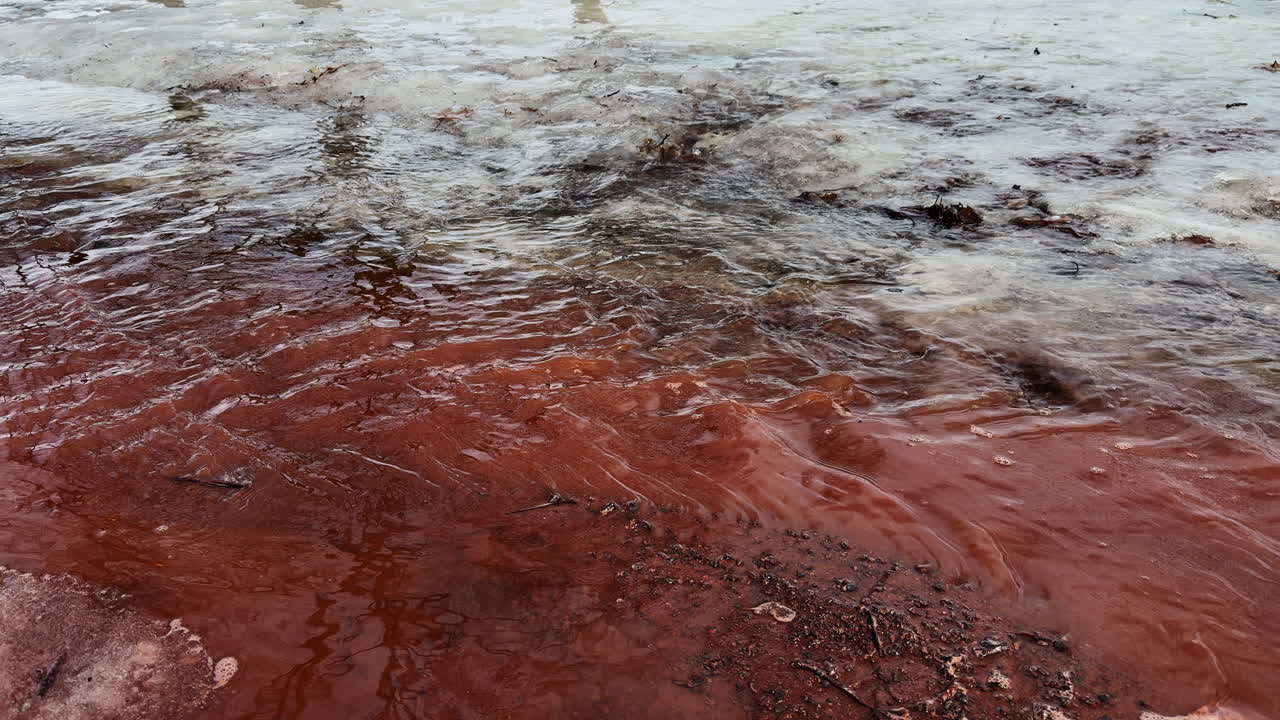 Di akhir musim dingin, aliran deras lelehan salju mengubah jalur berlumpur merah menjadi sungai sementara, menampilkan transisi yang jelas dan sangat terlihat dari tanah beku ke awal musim semi