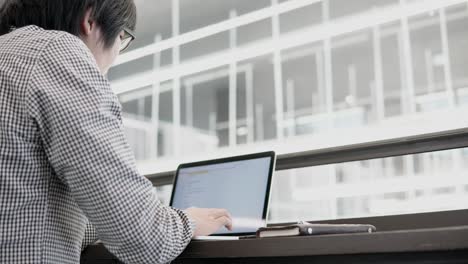 young asian business man using laptop computer in working space with smartphone and notebook on wooden desk. male hand typing on laptop keyboard. freelance lifestyle in digital age concept.