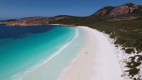 4k drone video of a couple running along the white sand beach next to the crystal clear blue ocean at thistle cove, esperance wa