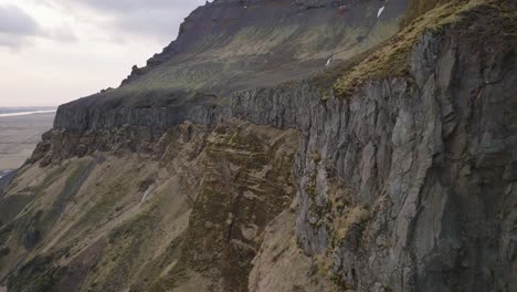 Aerial-cinematic-view-of-mountain-rock-formations-and-steep-cliffs,-with-melting-snow,-on-a-moody-evening-in-Iceland