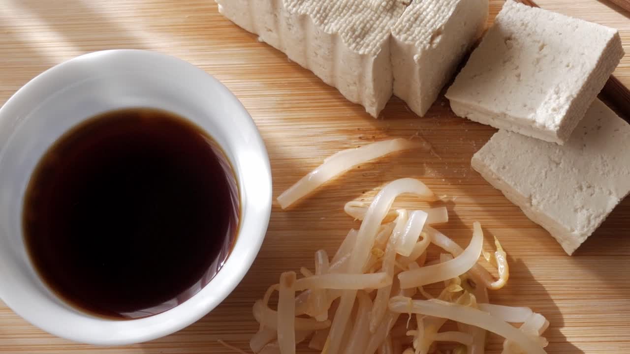 Tofu, bean sprouts and soy sauce on wooden board in warm kitchen light