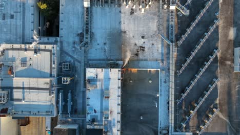 Top-down-aerial-view-of-industrial-factory-rooftop-with-smokestacks,-HVAC-units,-and-solar-panels