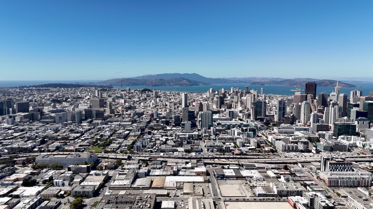 A wide panoramic aerial view of downtown San Francisco, showcasing the extensive cityscape with high-rise buildings, the Bay Area, and landmarks like the Golden Gate Bridge in the distance.